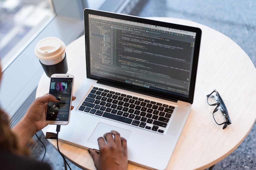 A professional woman intently working on her laptop while using her smartphone